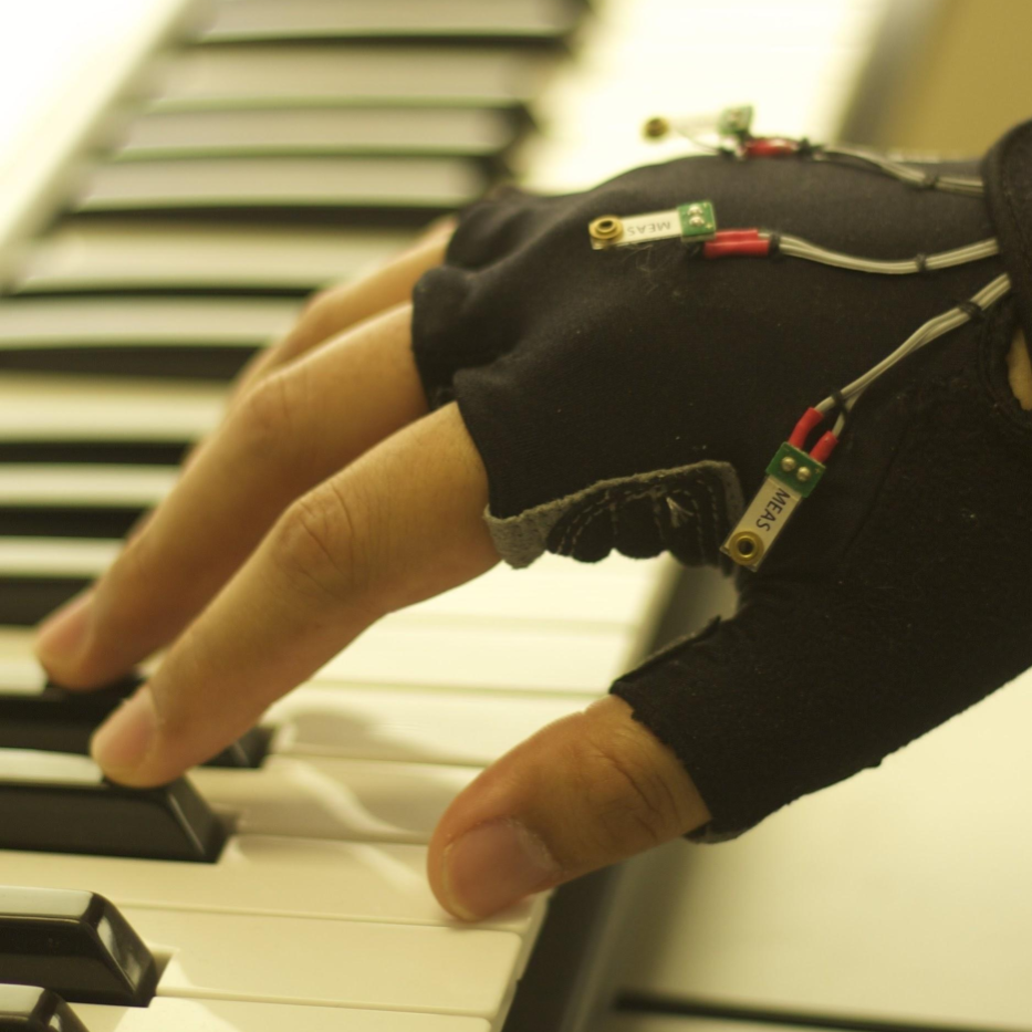 Hand touching piano keys while wearing a glove with electronics on it